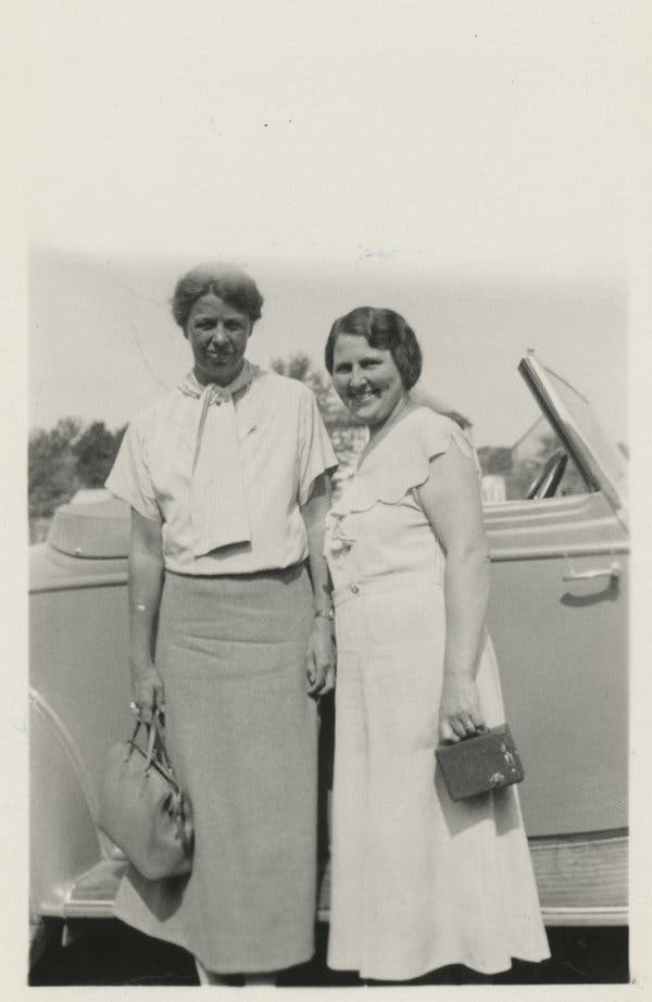Eleanor and Lorena standing close in front of a car. They are both smiling at the camera, Lorena more serious.