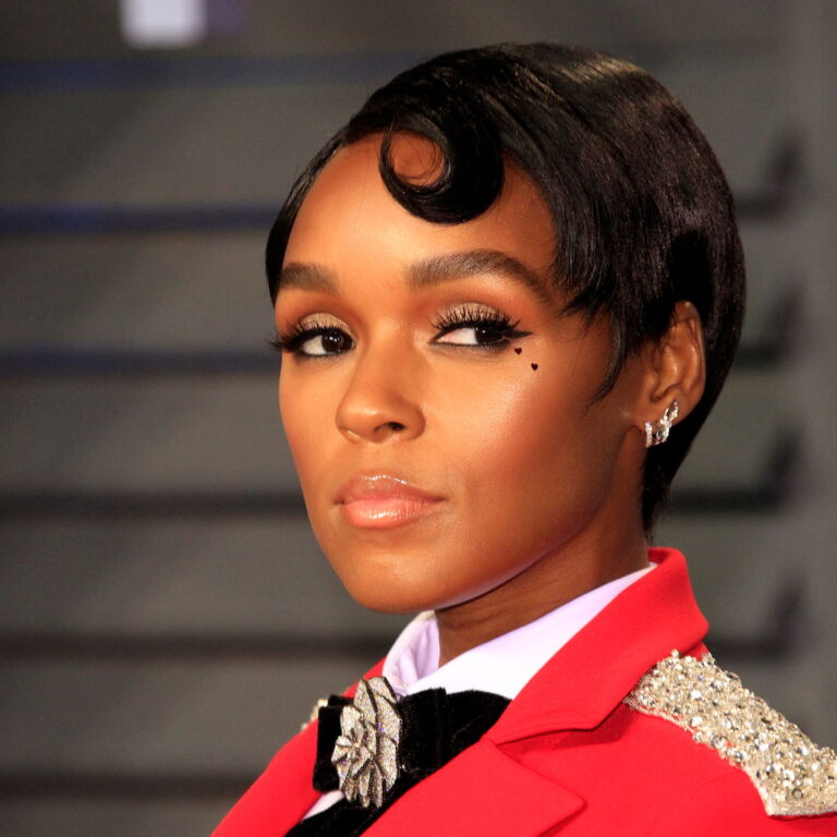 Janelle looking to the side wearing a sharp red suit.