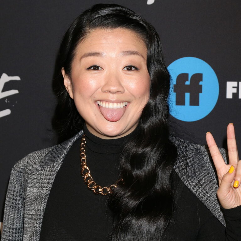 Sherry smiling with her tongue out and a holding the peace sign during a carpet event.
