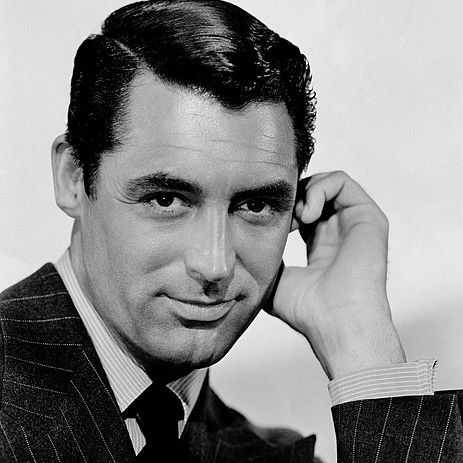 Black and white image of Cary smiling coyly with a hand to his side.