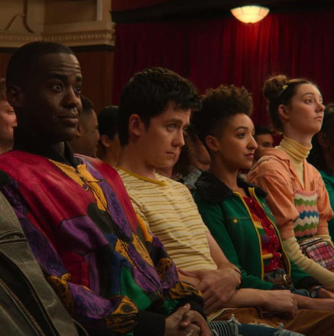 The cast of Sex Education with their colorful clothing sitting bored in the school theater.