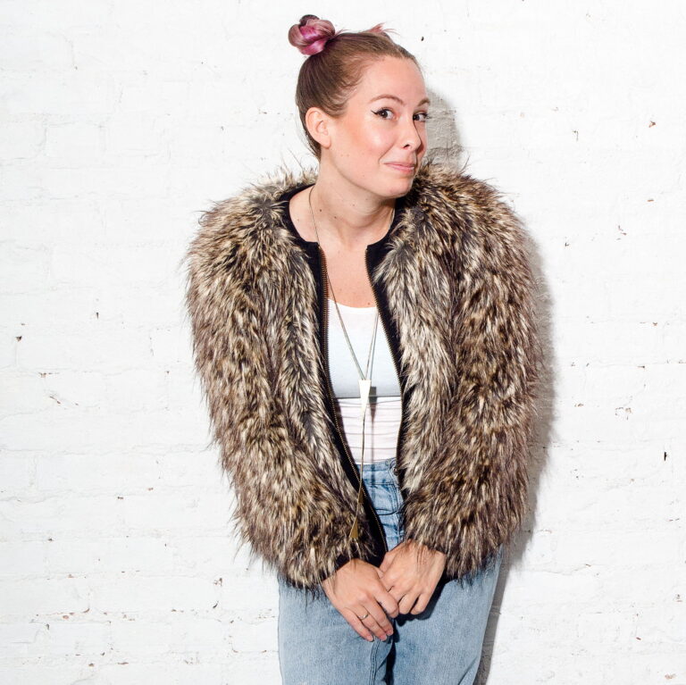 Image of Amber Rollo wearing a puffy jacked and hair in buns, against a white background looking coyly at the camera.