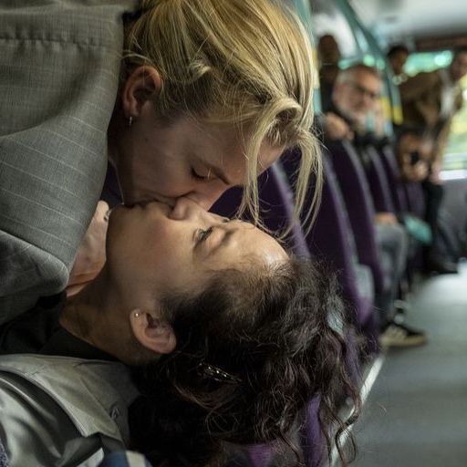 Villanelle and Eve laying on a bus seat kissing while the other passengers are looking at them.