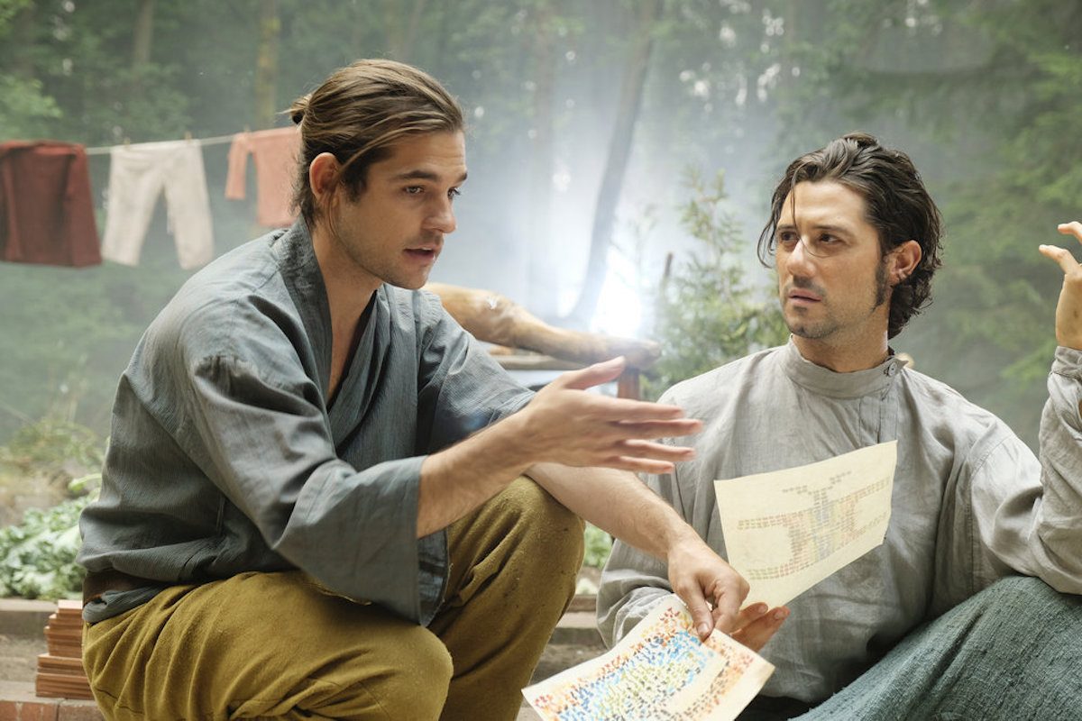 Quentin y Eliot discutiendo planes con un mapa, mientras est&aacute;n sentados en el suelo en el bosque.