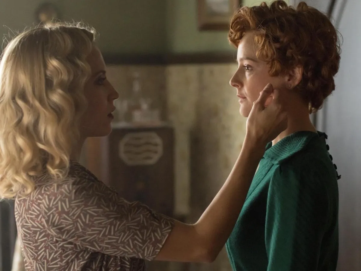 Carlota caressing the face of another woman, both look into eachothers' eyes.