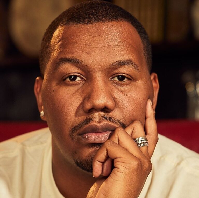 Trevon Free looking at the camera in the foreground with a hand on his cheek.