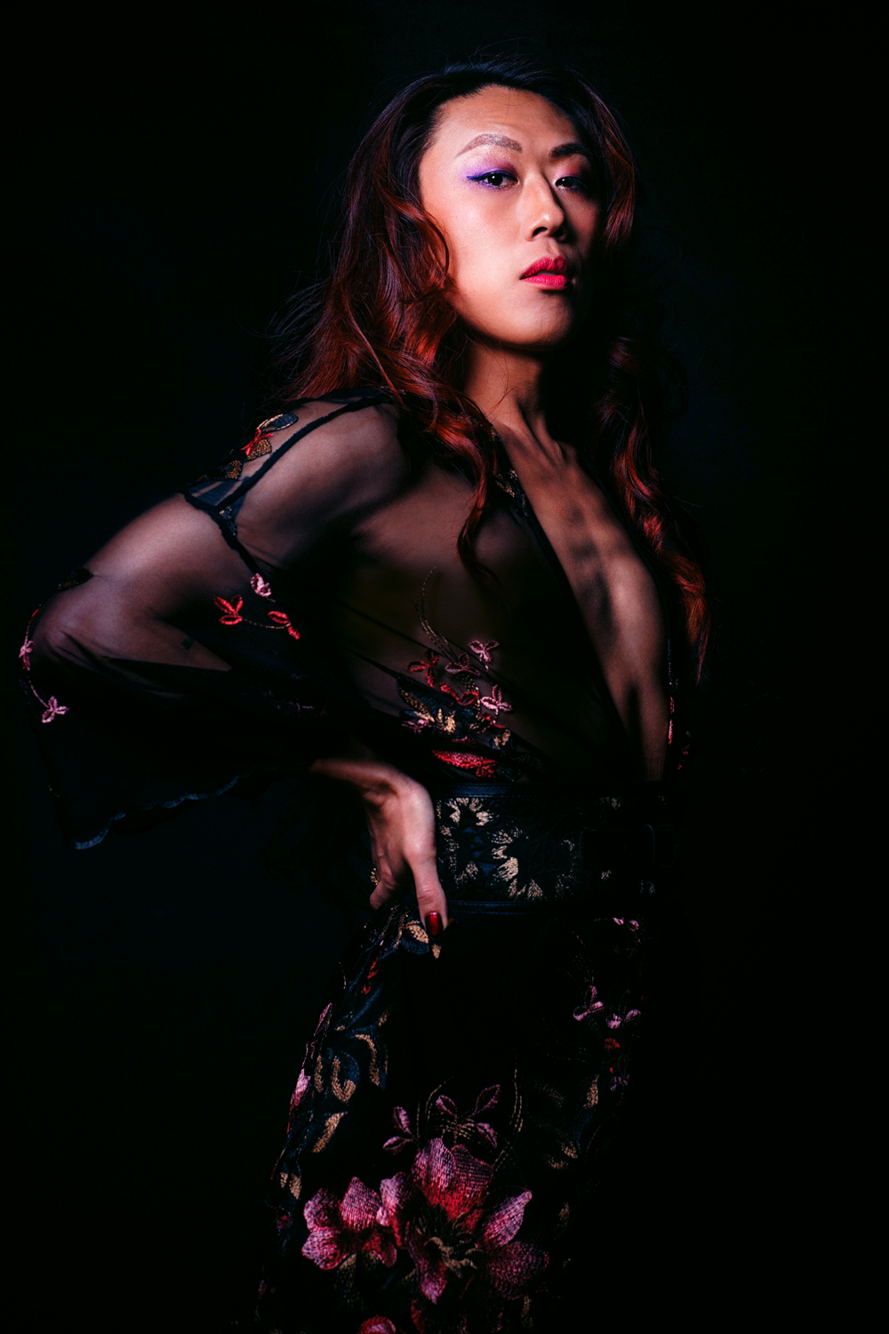 Una foto profesional de Nicky con un vestido floral transparente y posando con la cabeza en alto con un fondo oscuro.