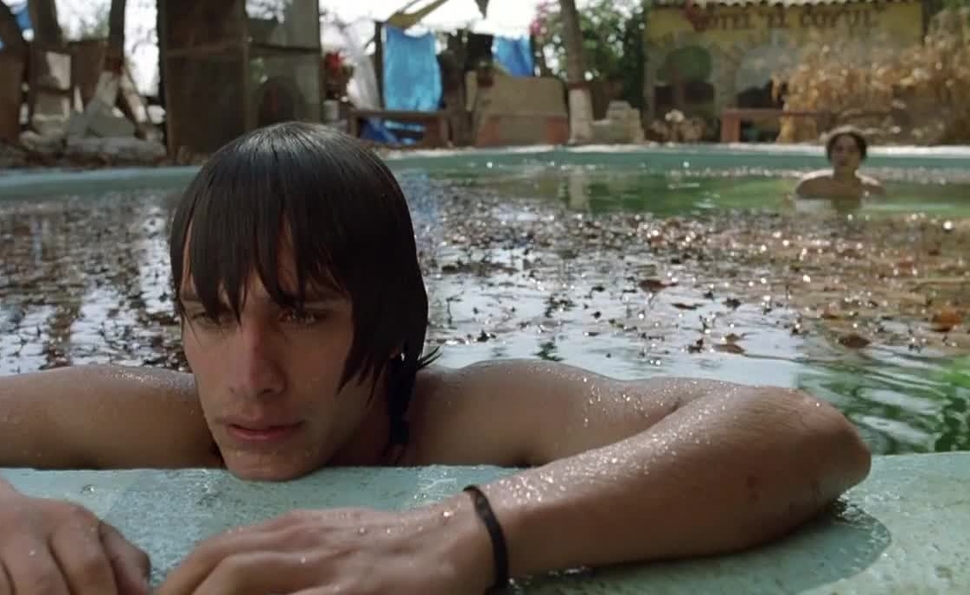 Julio sostenidose en la esquina de la alberca con expresion molesta. Mientras tenoch lo observa.