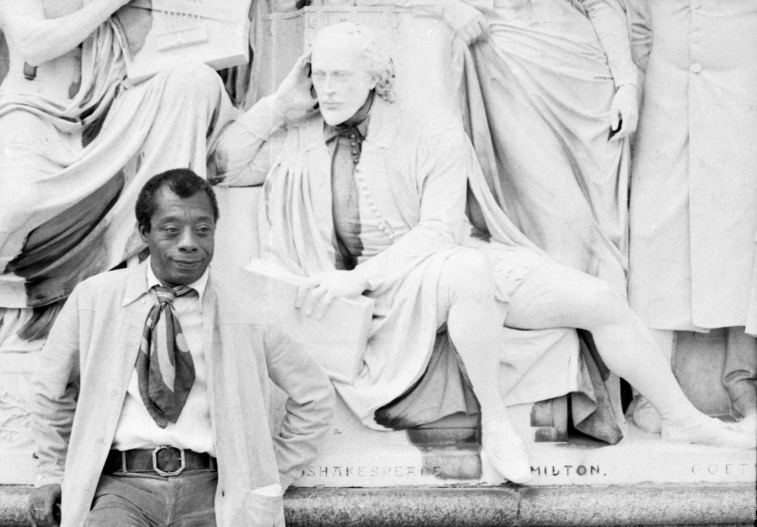 James Baldwin en el Albert Memorial con una estatua de Shakespeare, tiene las manos detr&aacute;s de la espalda.