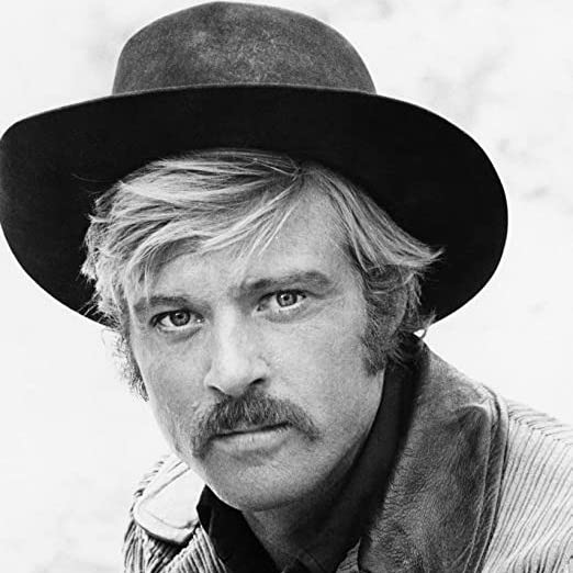 Sundance wearing a hat and jacket with a serious look.