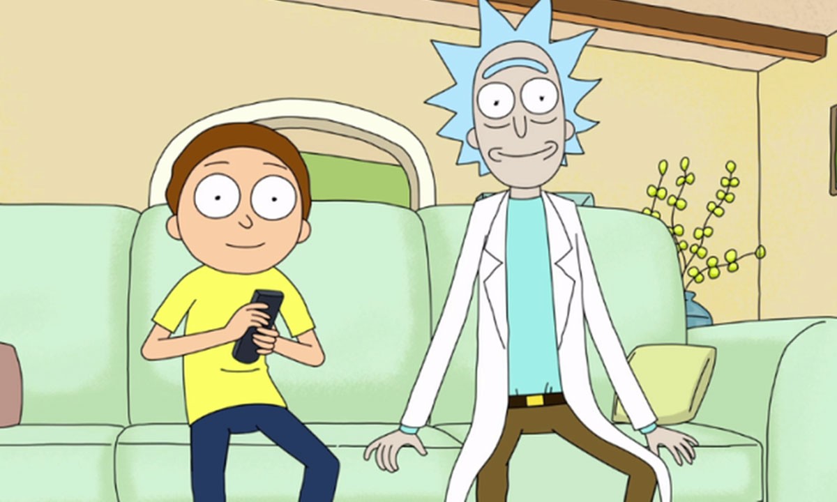 Rick and Morty sitting in their couch smiling staring at the camera with Morty holding the control.