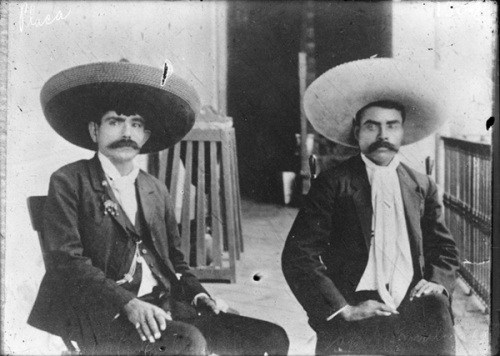 Zapata e Ignacio sentados juntos con chaqueta y sombrero.