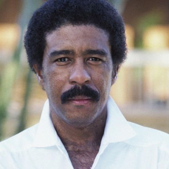 Richard Pryor, wearing a white button up and smiling gently.
