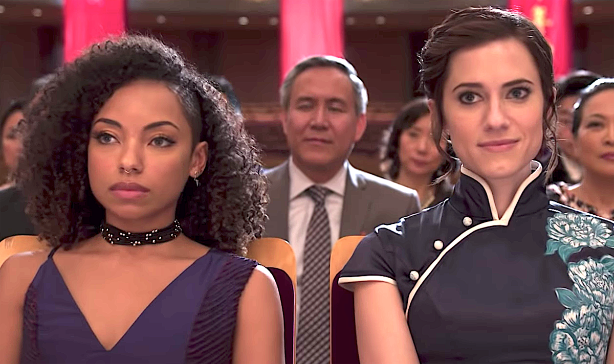 Charlotte and Lizzie watching a performance together dressed up. Charlotte is smiling and Lizzie is serious.