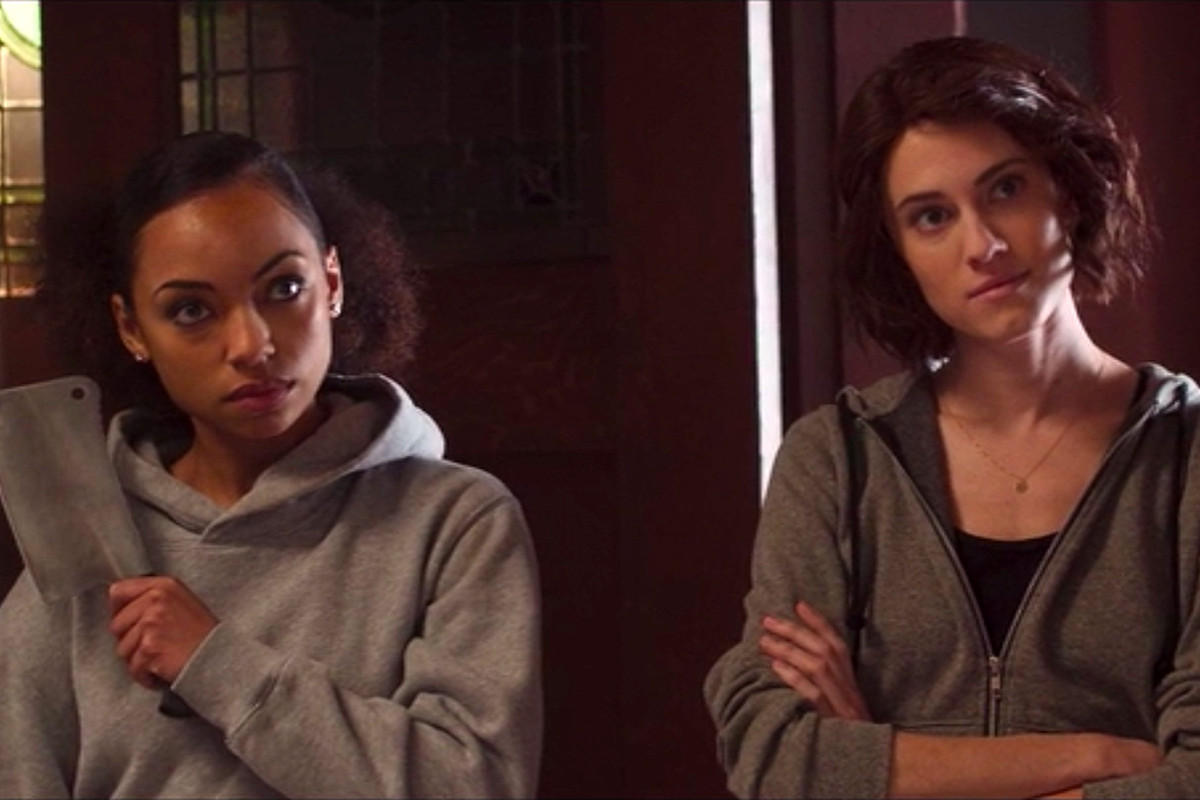 Charlotte and Lizzie looking at someone off screen smiling menacingly, Lizzie is holding a cleaver.