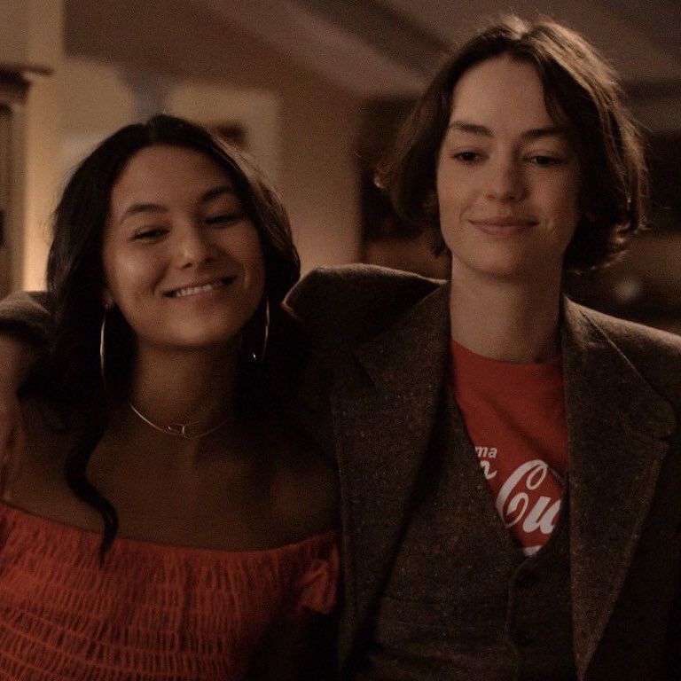 Image of Izzie and Casey, with Casey with her arm around Izzie's shoulder at a house while smiling to someone off camera.
