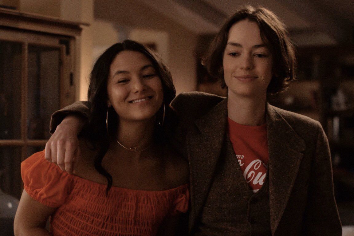 Image of Izzie and Casey, with Casey with her arm around Izzie's shoulder at a house while smiling to someone off camera.