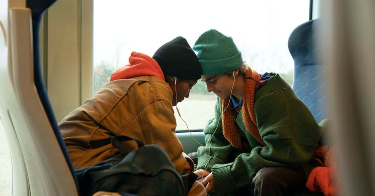 Caitlin and Fraser pressing their heads together sitting at a train sharing headphones.