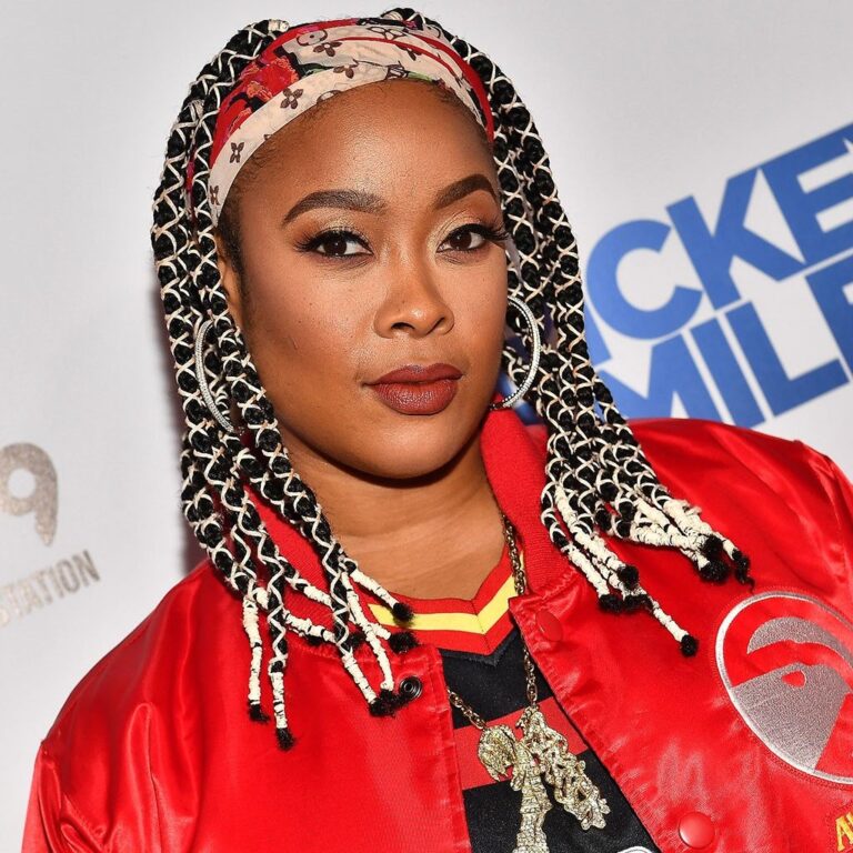 Da Brat wearing bright colored clothing and her hair in braids with a head wrap, looking at the camera.