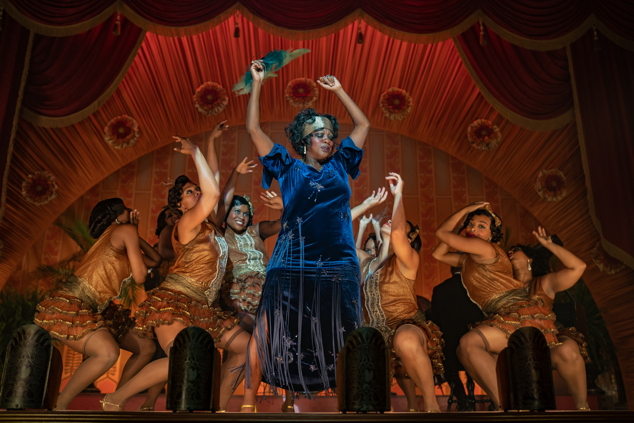 Ma Rainey posing with her dancers behind her also in a pose, lifting their hands in the air while crouching.