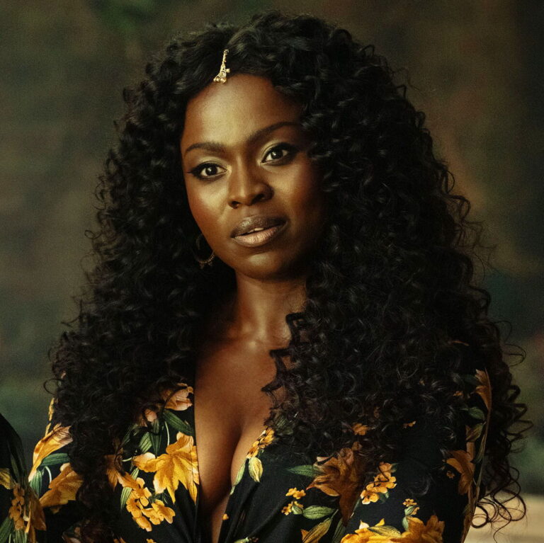 Bilquis, depicted as a beautiful black woman with large curly hair, looks serious ahead of her.