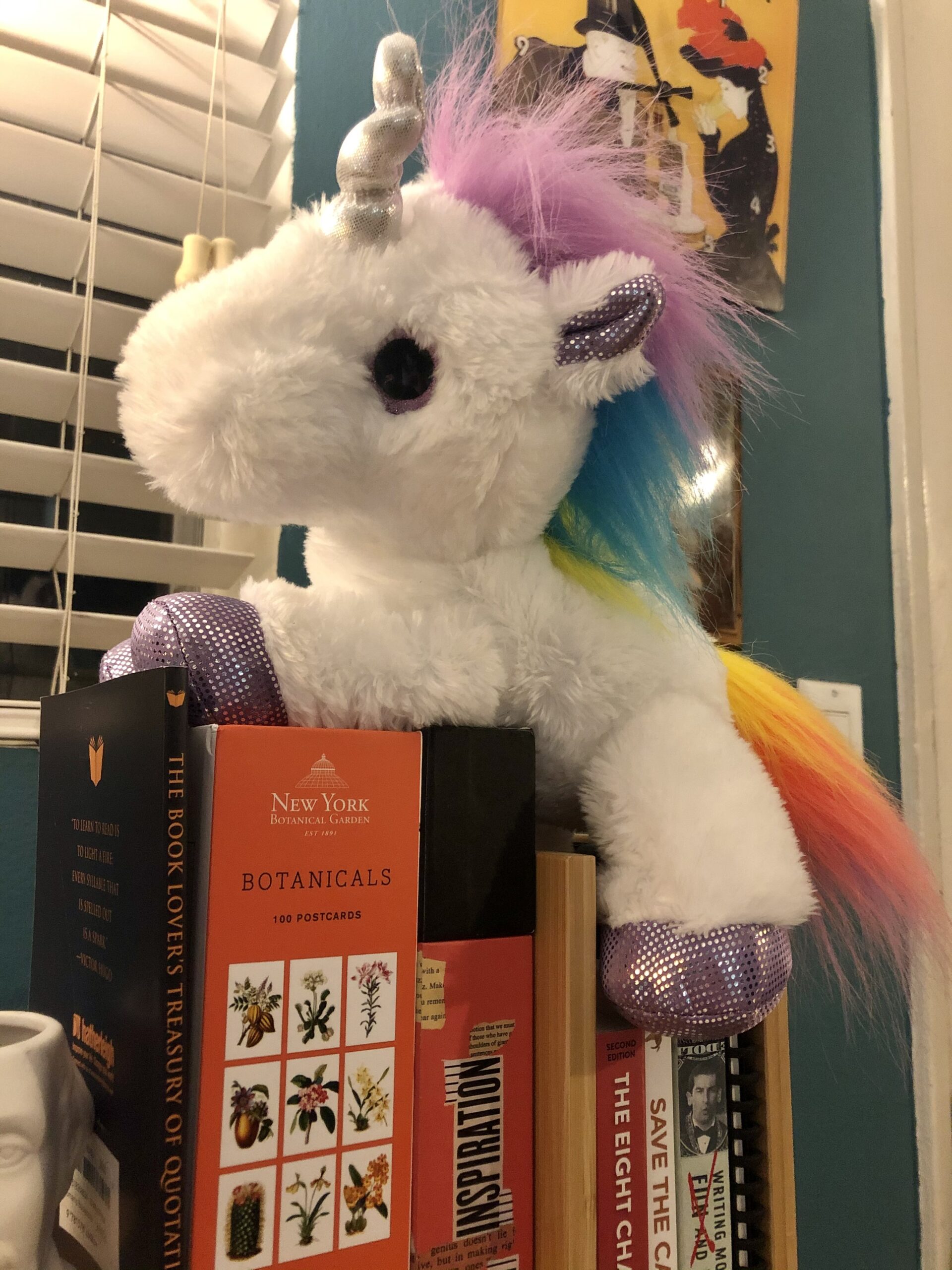 A plush Unicorn sitting on a pile of books.