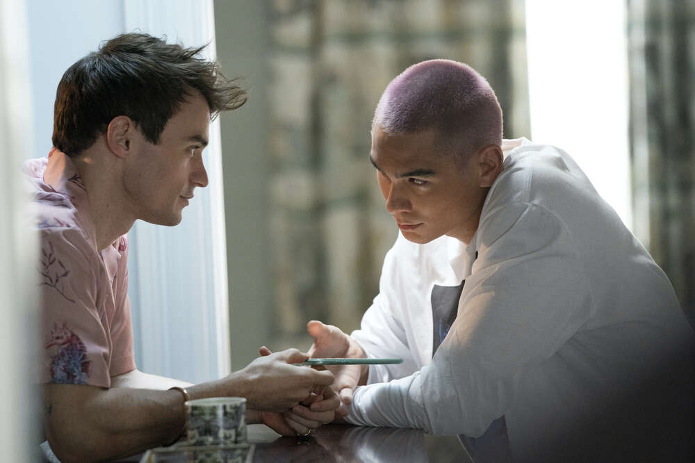 Aki y Max sentados sobre una mesa mientras se miraban a los ojos con tensi&oacute;n en el aire.