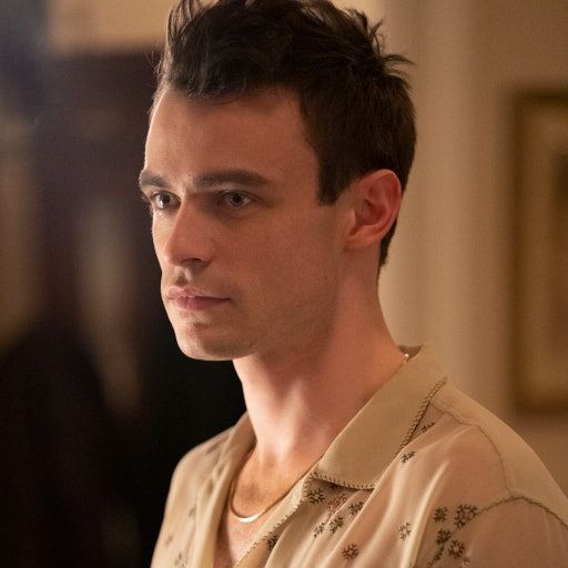 Max Wolfe wearing a button up shirt and necklace, with a serious look on his face.