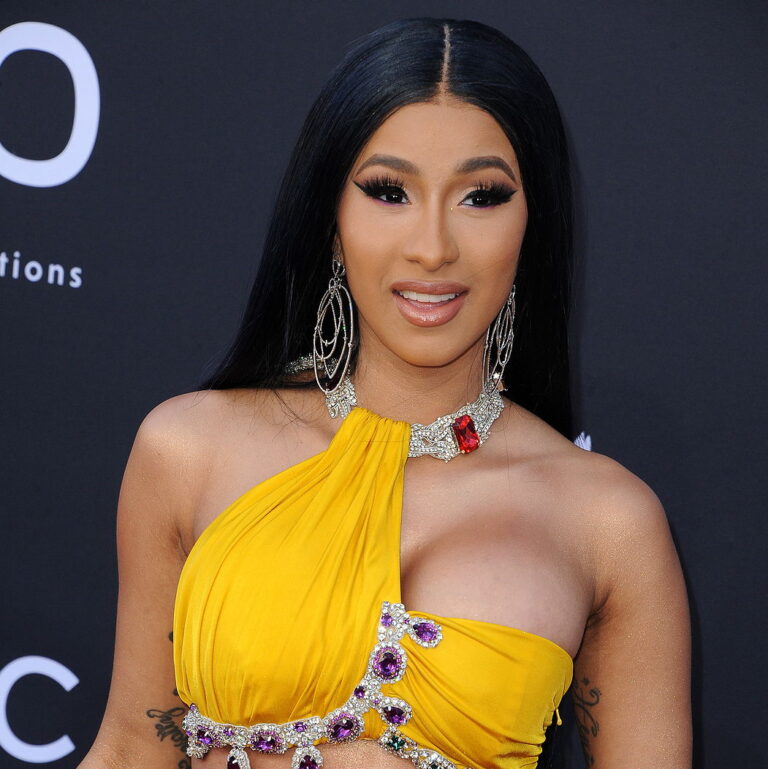 Cardi B in a red carpet event wearing a yellow dress and smiling.