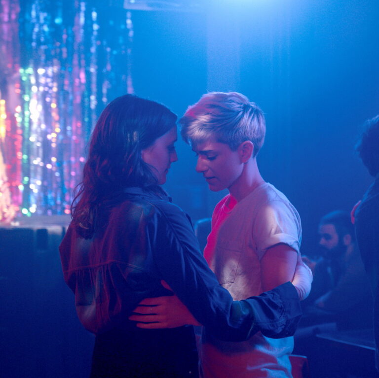 Mae and George holding eachother close dancing slowly under purple and dim lights.