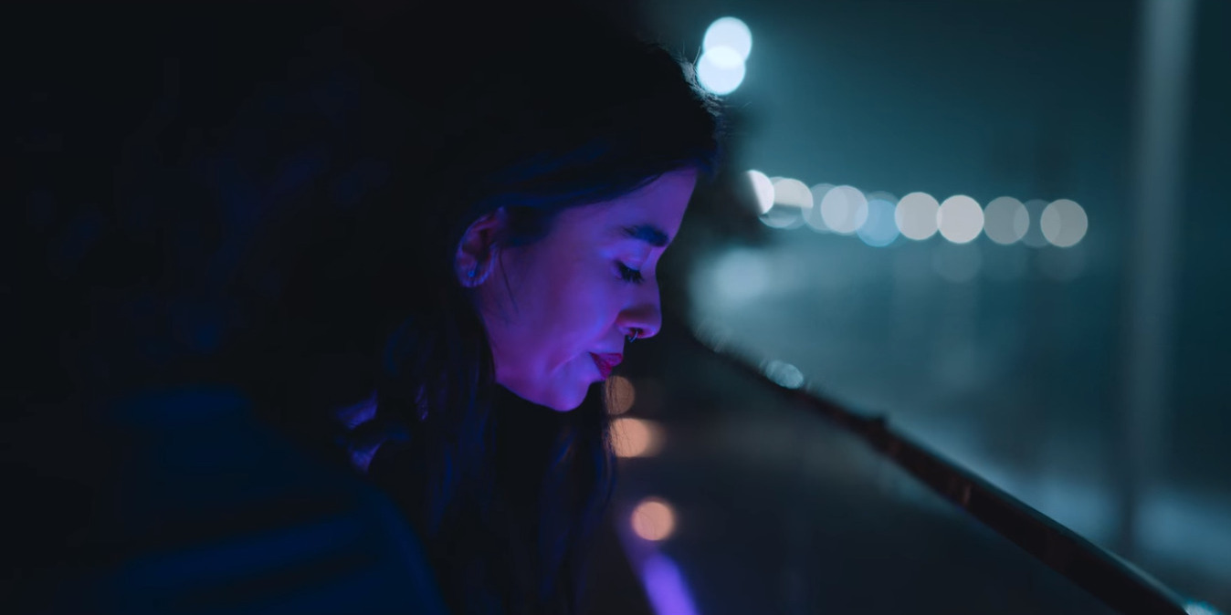 La silueta de un personaje con la cabeza mirando hacia abajo y los ojos cerrados, con una luz violeta iluminando su rostro.