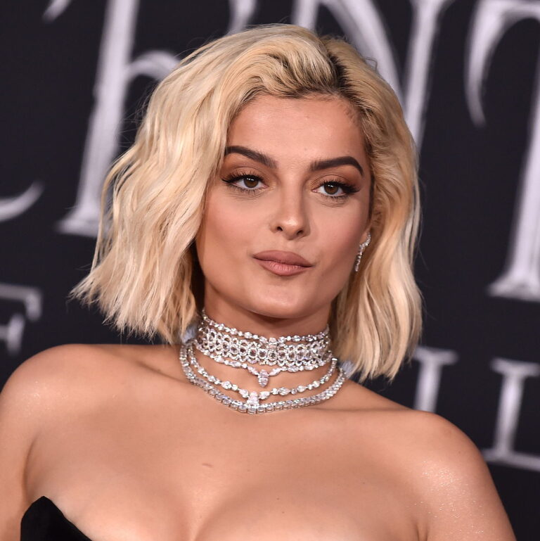 Bebe Rexha at a carpet event looking glamorous with a pearl necklace and a serious expression.