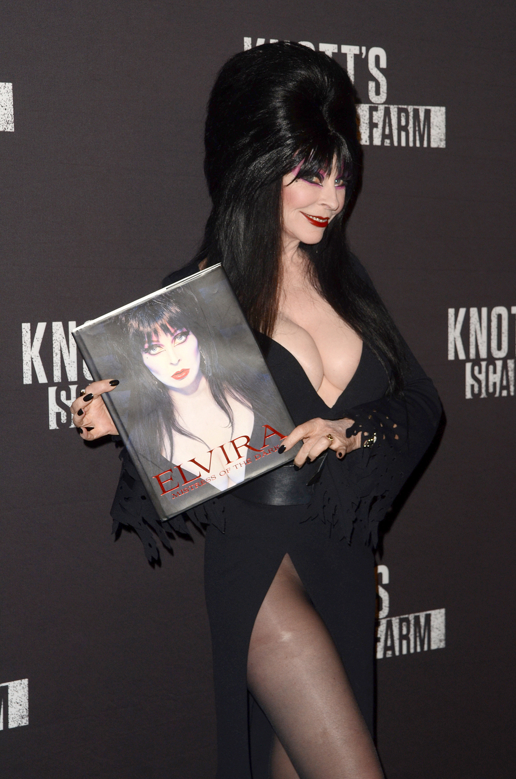 Elvira at the 2016 Knott's Scary Farm at Knott's Berry Farm holding her book and smiling.