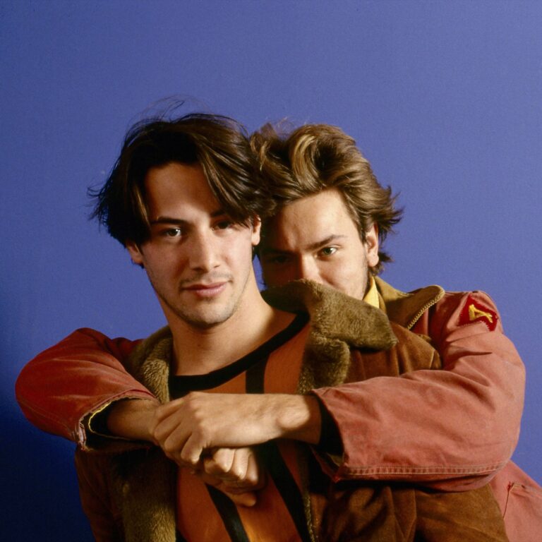 Mikey hugging Scott from behind and hides part of his face as well. They are in front of a purple backdrop.