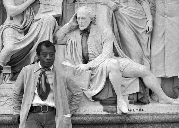 Fotografía en blanco y negro de Jams Baldwin posando con la estatua de Shakespeare.