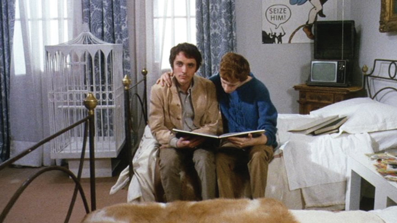 The Visitor reading something with Prieto in his room. Prieto has his hand around The visitor's shoulder.