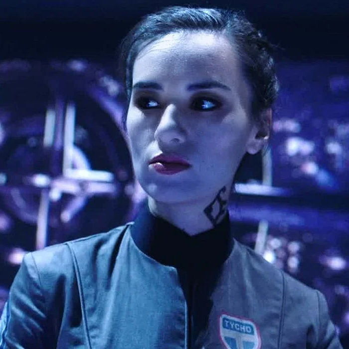 Camina looking to the side while wearing her uniform and a serious expresion.