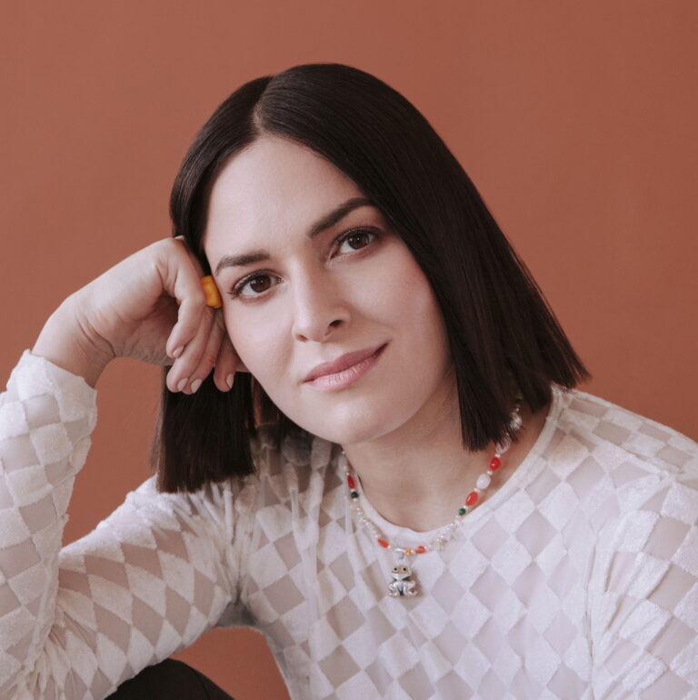 Jen Winston resting her head on her hand smiling wearing a checkered shirt.