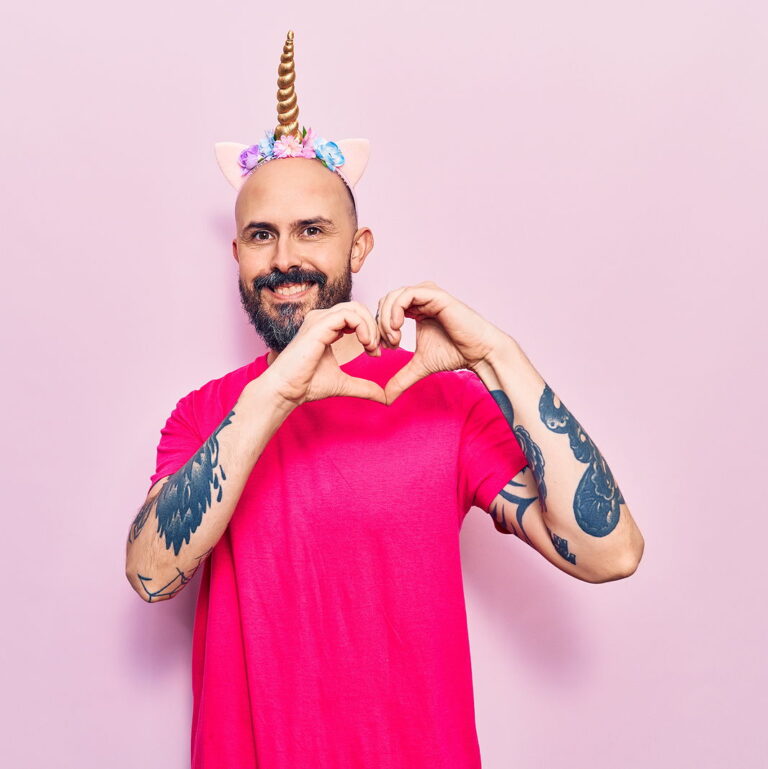 A young handsome man wearing unicorn diadem smiling doing heart symbol shape with hands