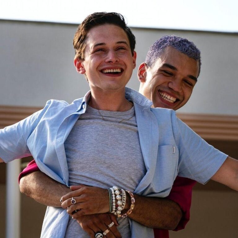 Chester hugging Nathan from behind while Nathan stretches his arms. Both are laughing.