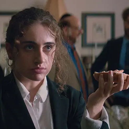 Danielle holding a bagel in one hand looking to the side while Jewish relative are in the background.
