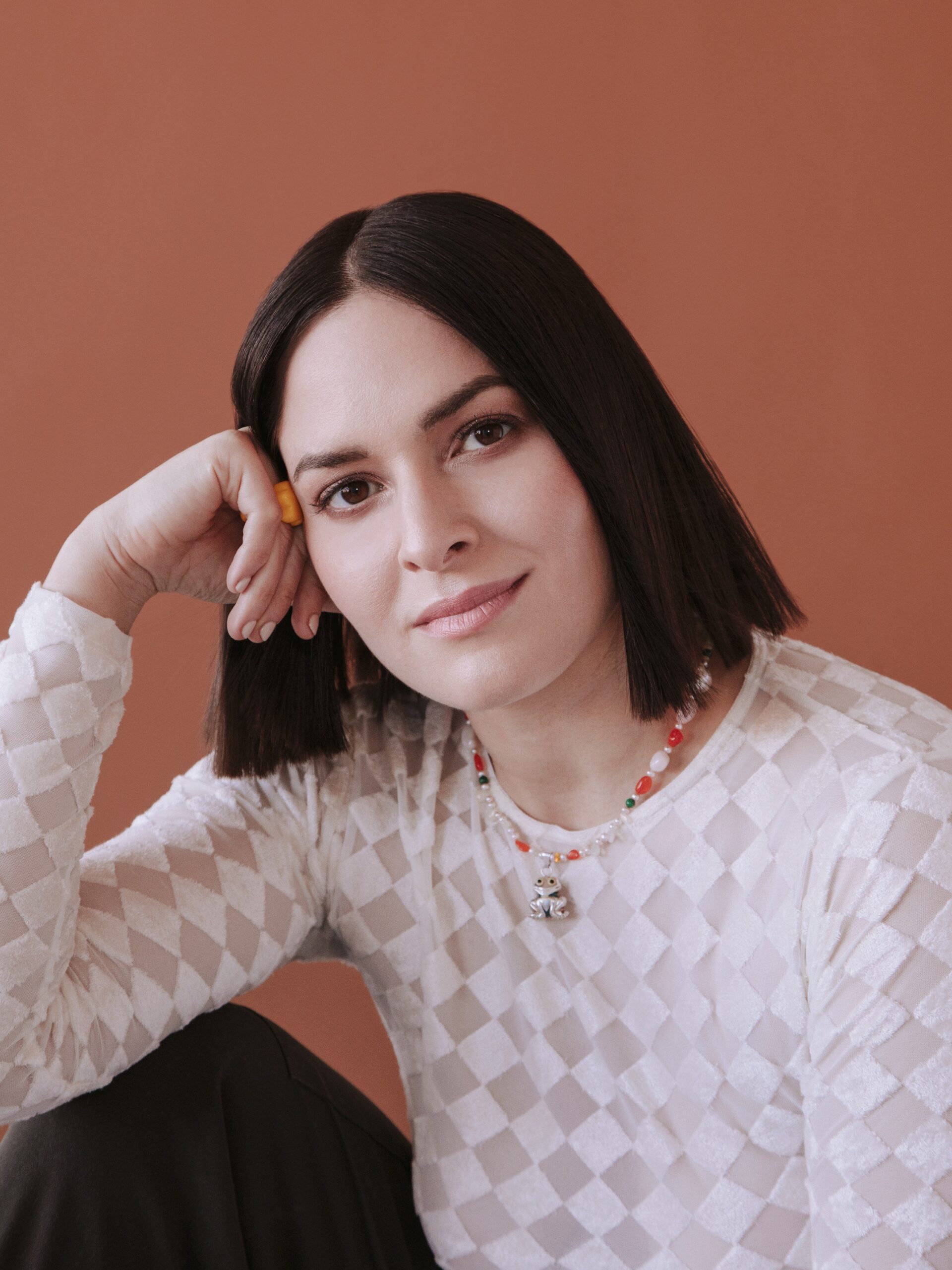 Jen Winston resting her head on her hand smiling wearing a checkered shirt.