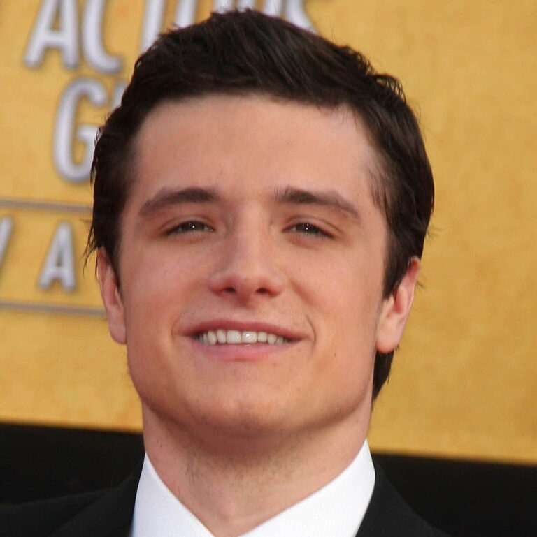 Josh Hutcherson smiling at a carpet event for Hunger Games with his co host in a suit.