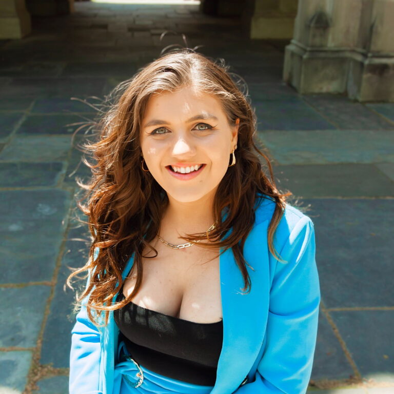 Esmé smiling standing on steps on a sunny day.