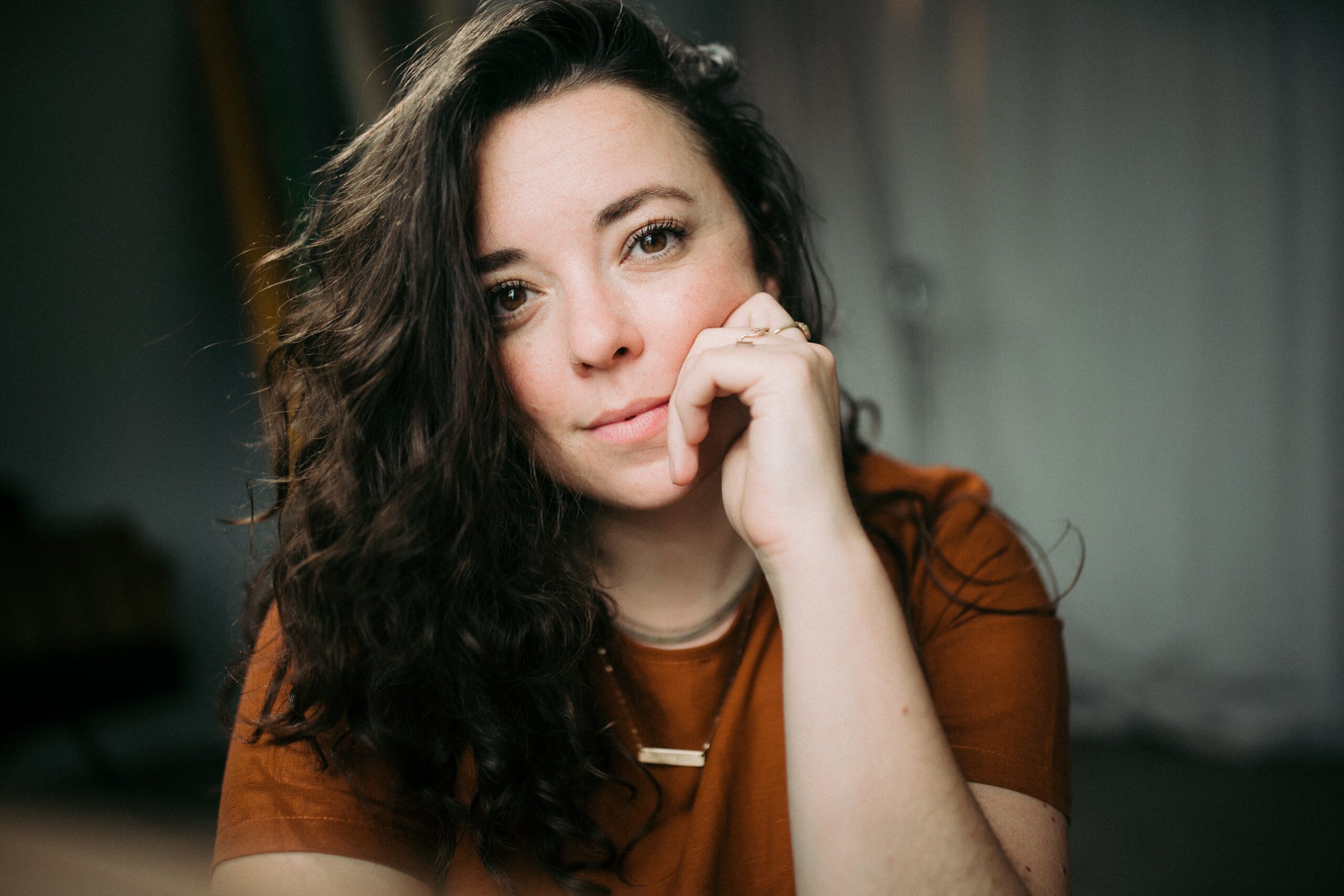 Retrato de Becca con el cabello hacia un lado y una mano en la barbilla sonriendo.