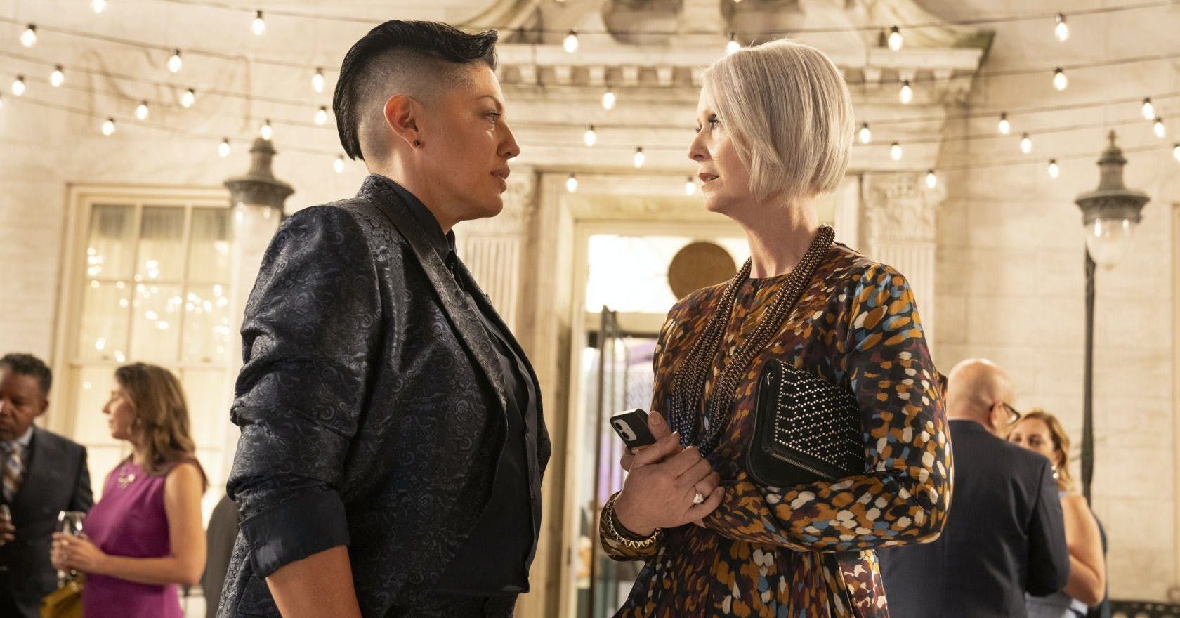 Miranda and Che talk with serious expressions. they are dressed formally while at an event.