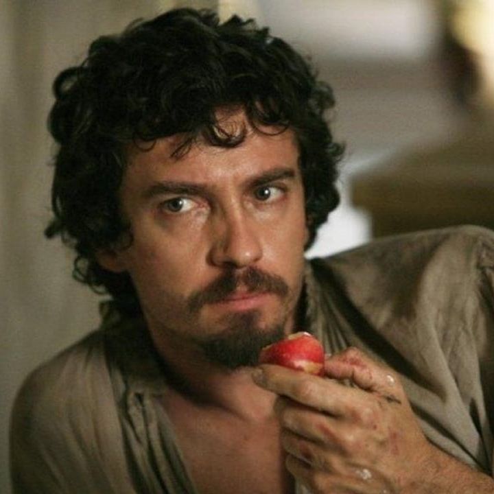Caravaggio leaning on his shoulder looking at someone out of frame with a serious expression, eating an apple.
