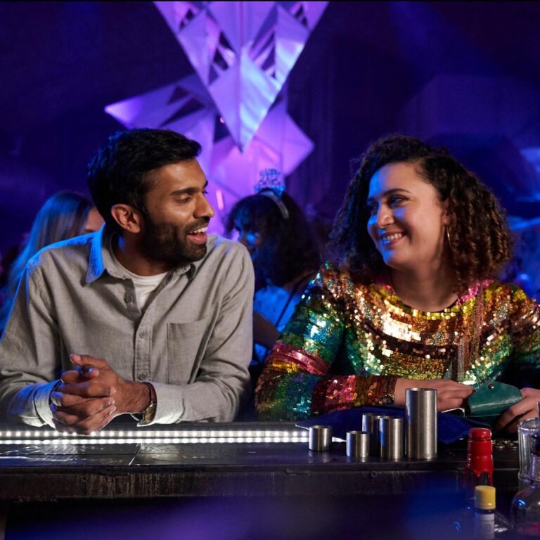 Jessie talking to Tom at the new years eve bar. Both are smiling.