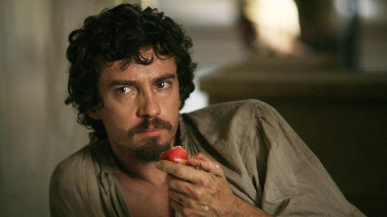 Caravaggio leaning on his shoulder looking at someone out of frame with a serious expression, eating an apple.