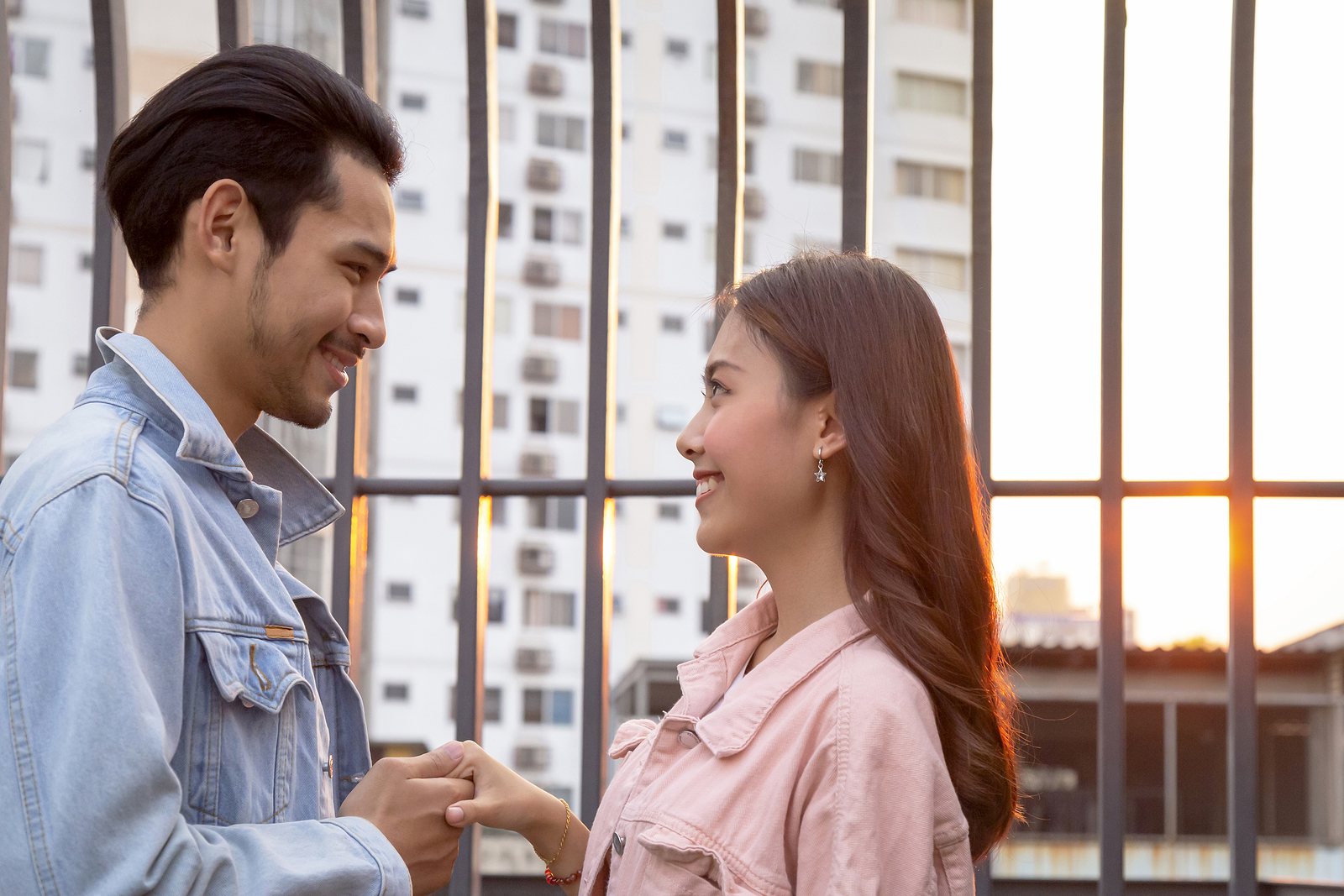 Un joven asi&aacute;tico y una mujer se paran uno frente al otro. Est&aacute;n sosteniendo una mano y sonriendo.
